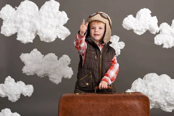 Αγόρι ντυμένος σαν ένα αεροπλάνο πιλοτικά περίπτερο μεταξύ τα σύννεφα με παλιά βαλίτσα και να παίζει με το χειροποίητο αεροπλάνο — Φωτογραφία Αρχείου