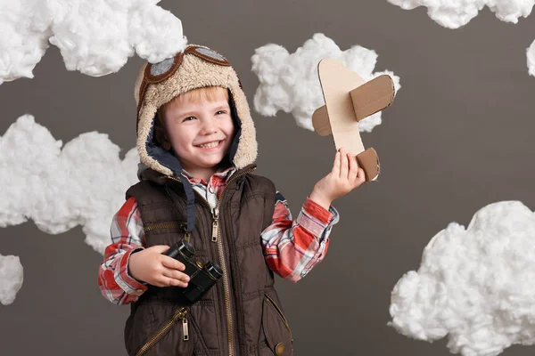 Αγόρι ντυμένος σαν ένα αεροπλάνο πιλοτικά στέκεται ανάμεσα στα σύννεφα και να παίζει με το χειροποίητο αεροπλάνο — Φωτογραφία Αρχείου