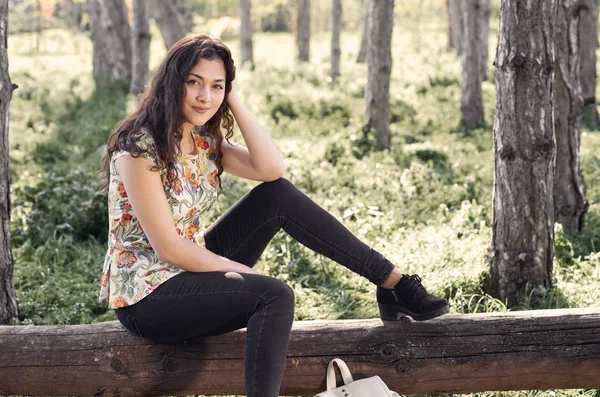 Szczęśliwa młoda dziewczyna siedzi na dziennik w lesie, jasne światło słoneczne wokół, piękno przyrody na wiosnę — Zdjęcie stockowe