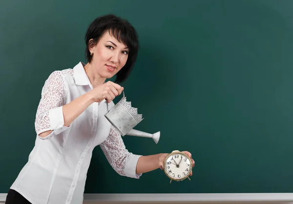 Woman with watering can and clock on blackboard background, blank space for your drawing — Stock Photo, Image