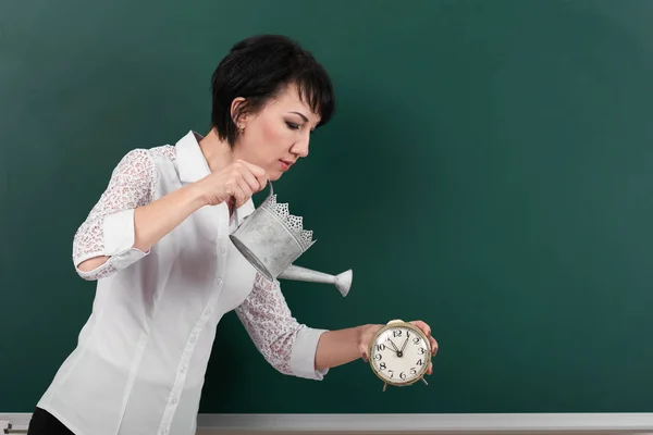 Woman with watering can and clock on blackboard background, blank space for your drawing — Stock Photo, Image