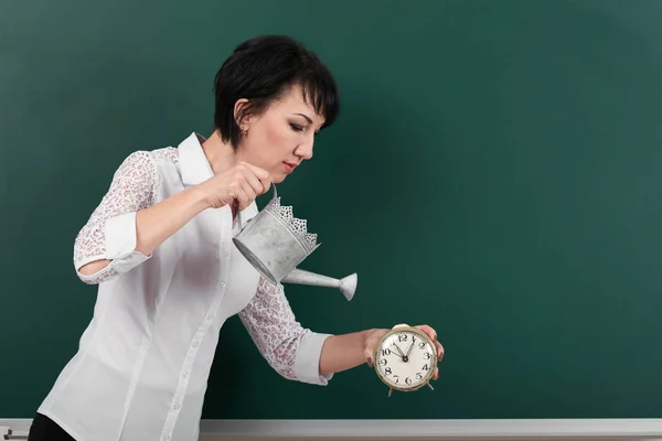 Mujer con regadera y reloj en el fondo de pizarra, espacio en blanco para su dibujo — Foto de Stock