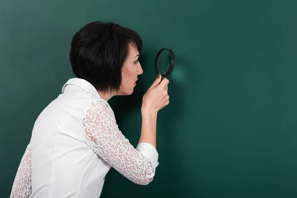 Una mujer mira a través de una lupa y busca algo, una pizarra como fondo, un concepto de educación y negocios —  Fotos de Stock