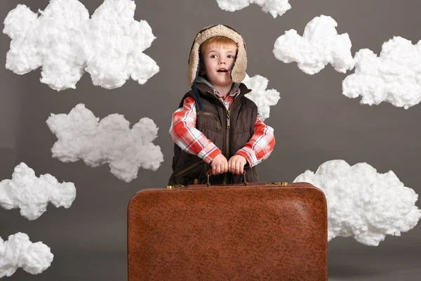 Αγόρι ντυμένος σαν ένα αεροπλάνο πιλοτικά περίπτερο μεταξύ τα σύννεφα με παλιά βαλίτσα και να παίζει με το χειροποίητο αεροπλάνο — Φωτογραφία Αρχείου