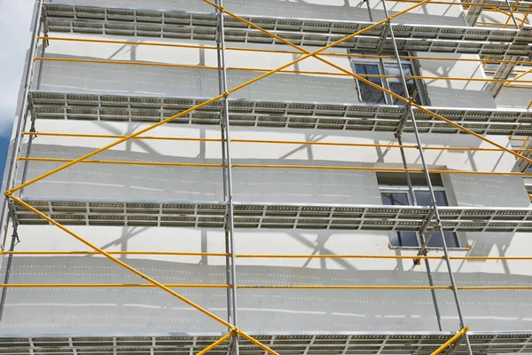 Échafaudage près d'une maison neuve, bâtiment extérieur, construction et réparation, mur blanc et fenêtre, tuyau jaune — Photo
