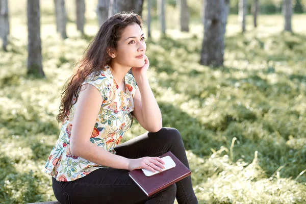 Happy young girl sitting on a log in the forest, bright sunlight around, beauty of nature in spring — Stock Photo, Image