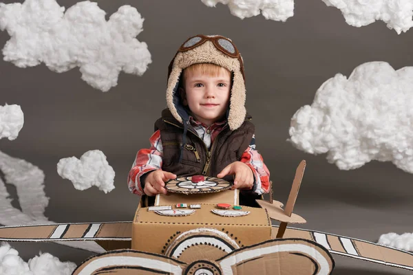 Το αγόρι που παίζει σε ένα αεροπλάνο από χαρτόκουτο και ονειρεύεται να γίνει πιλότος, σύννεφα, βαμβάκι σε ένα γκρίζο φόντο — Φωτογραφία Αρχείου