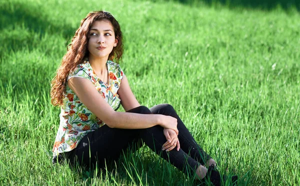 Piękna dziewczyna siedzi na Polanie w lesie, jasne słońce i cienie na trawie — Zdjęcie stockowe