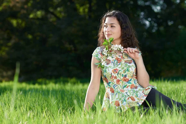 Hermosa chica sentada en un claro en el parque, sol brillante y sombras en la hierba —  Fotos de Stock