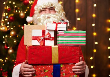 Noel Baba bir sürü hediyeyle poz veriyor, kapalı bir yerde süslü Noel ağacının yanında oturuyor - Mutlu Noeller ve mutlu tatiller!
