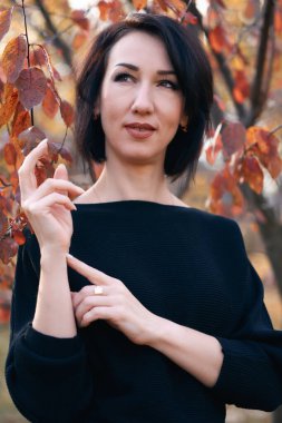 Sonbaharda bir şehir parkında duran ve poz veren zarif bir kadın.