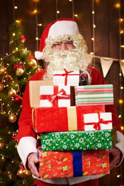 Noel Baba bir sürü hediyeyle poz veriyor, kapalı bir yerde süslü Noel ağacının yanında oturuyor - Mutlu Noeller ve mutlu tatiller!
