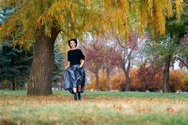 Hermosa mujer elegante corriendo en un parque de la ciudad en otoño, árboles de color amarillo brillante y rojo —  Fotos de Stock