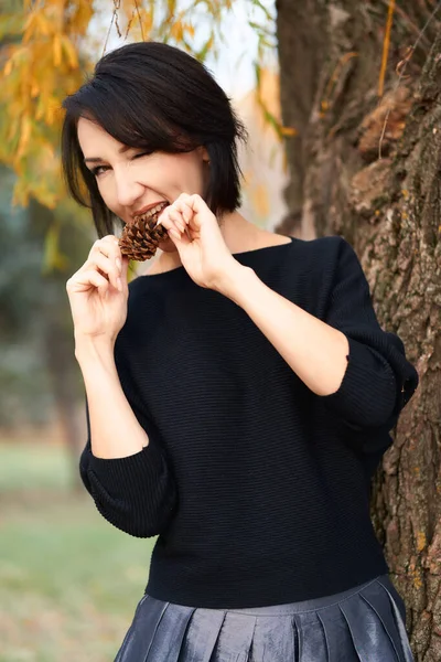 Красива елегантна жінка розважається і їсть ялиновий конус в міському парку восени — стокове фото