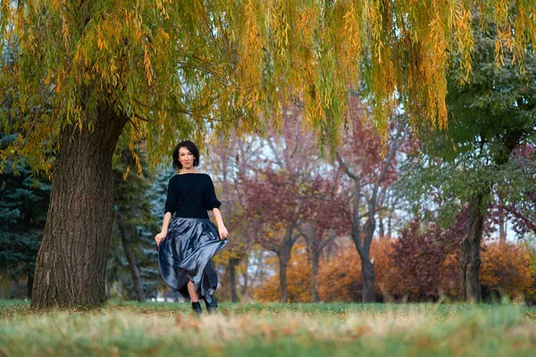 Hermosa mujer elegante de pie y posando cerca de un gran árbol amarillo en un parque de la ciudad en otoño —  Fotos de Stock