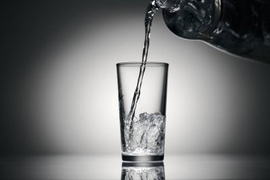 Karanlık bir arka planda bardağa köpüklü su dökmek