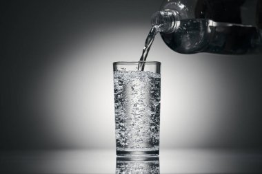 Karanlık bir arka planda bardağa köpüklü su dökmek