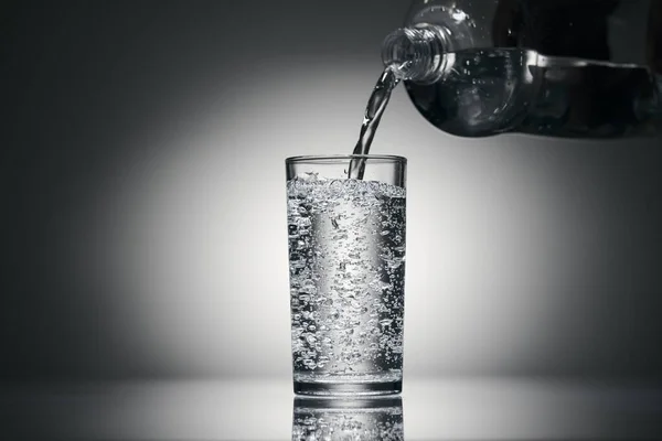 Wlewanie wody gazowanej do szklanki na ciemnym tle — Zdjęcie stockowe