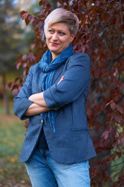 Sonbahar parkında poz veren güzel sarışın kadın, kot pantolon ve ceket giymiş.