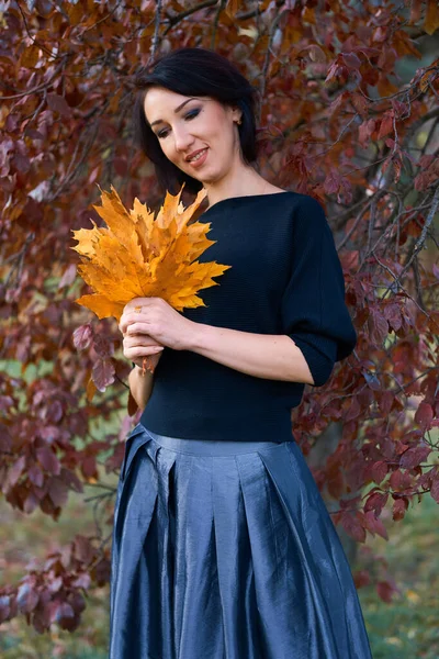 Mulher elegante bonita de pé e posando com buquê de folhas amarelas no parque da cidade de outono — Fotografia de Stock