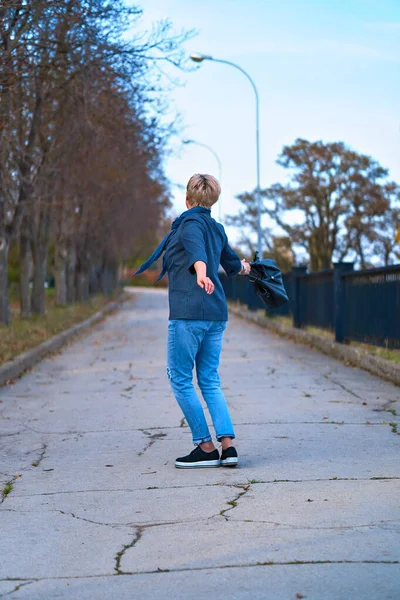幸せなブロンドの女性歩くと秋の都市公園を回転,青いジーンズとジャケットを身に着けています — ストック写真