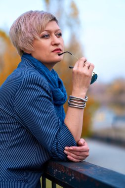 Sonbahar parkında poz veren güzel sarışın kadın, kot pantolon ve ceket giymiş.