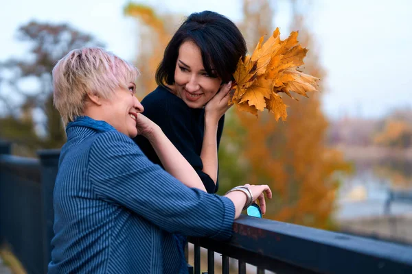 Zwei Freundinnen unterhalten sich und posieren im herbstlichen Stadtpark. schöne erwachsene Frau, blond und brünett. — Stockfoto