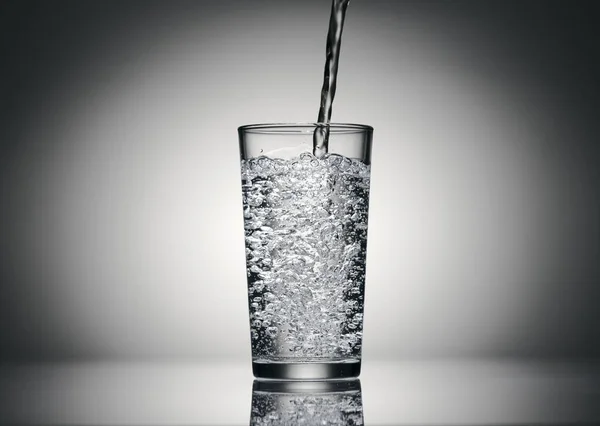 在深色底色的玻璃杯中倒入晶莹的水 — 图库照片
