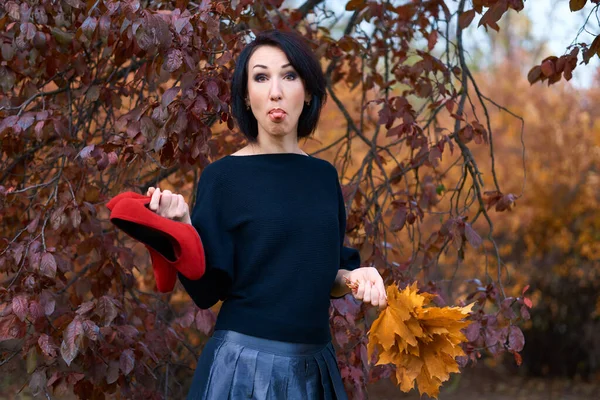 Beautiful elegant woman having fun and posing with bouquet of yellow leaves and red shoes in autumn city park — Stock Photo, Image
