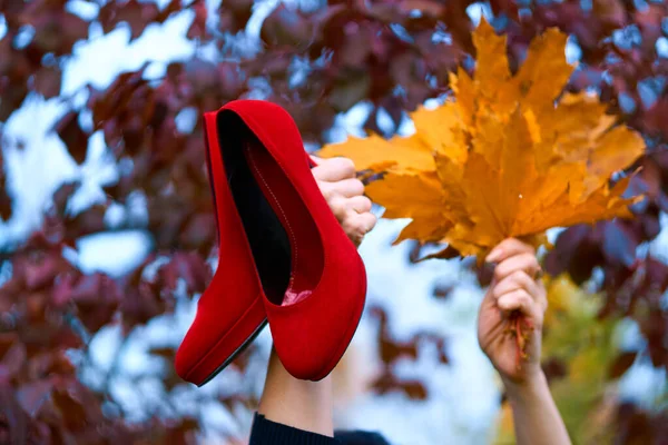 Woman raising her hands with bouquet of yellow leaves and red shoes in autumn city park — Stock Photo, Image