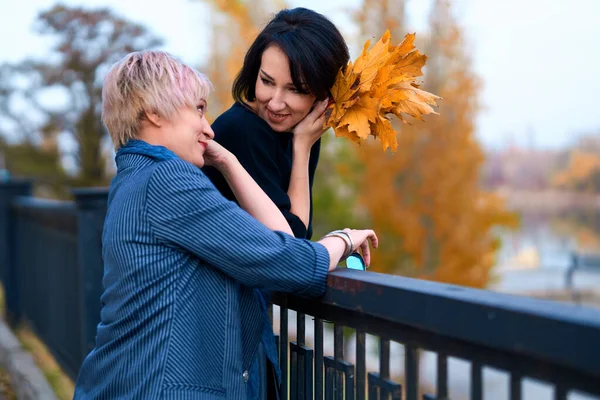 Dvě přítelkyně si povídají a pózují v podzimním městském parku. Krásná dospělá žena, blondýna a bruneta. — Stock fotografie