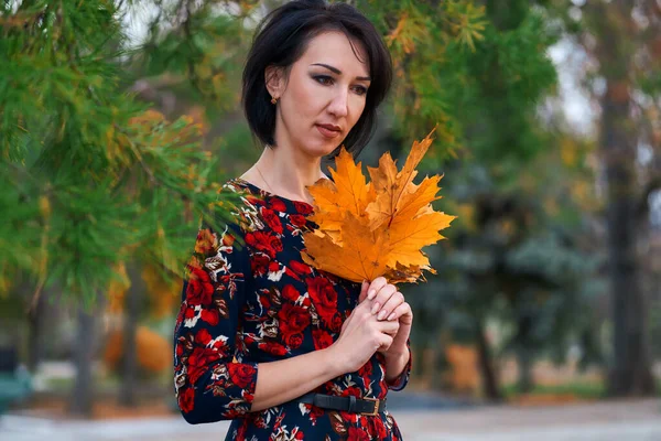Schöne elegante Frau steht und posiert mit einem Strauß gelber Blätter im herbstlichen Stadtpark — Stockfoto