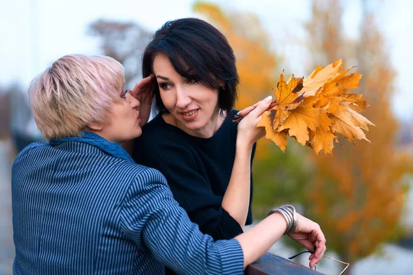 Dos novias hablando y posando en el parque de otoño de la ciudad. Hermosa mujer adulta, rubia y morena . — Foto de Stock