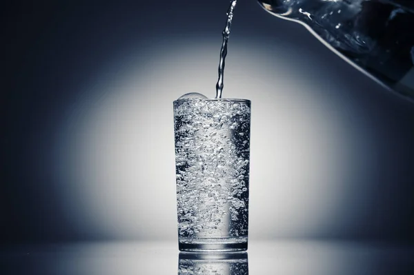 Gießen von sprudelndem Wasser in einem Glas auf dunkelblauem Hintergrund — Stockfoto