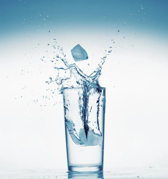 Um copo de água com respingo de cubo de gelo caindo, fundo branco, objeto isolado — Fotografia de Stock