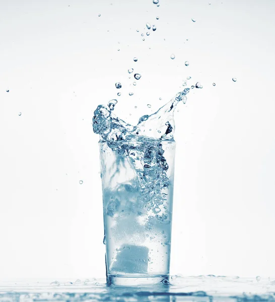 Un bicchiere d'acqua con spruzzi di ghiaccio caduta cubo, sfondo bianco, oggetto isolato — Foto Stock