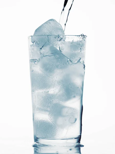 Derramando água em um copo cheio de cubos de gelo, fundo branco, objeto tonificado azul — Fotografia de Stock