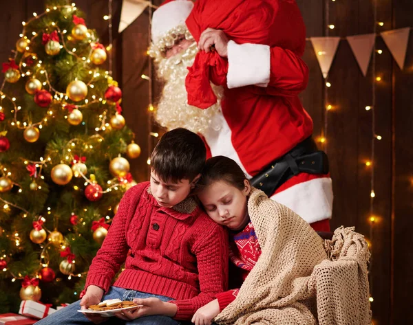 Los niños esperaron mucho tiempo a Santa, ahora se quedaron dormidos y Santa se dirige silenciosamente al árbol de Navidad para dar regalos - Feliz Navidad y Felices Fiestas ! — Foto de Stock