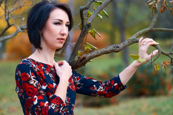 Beautiful elegant woman standing and posing near branches in autumn city park — Stock Photo, Image