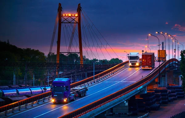 Samochód ciężarowy z przejazdami kontenerowymi po drodze, transport kolejowy, wagony towarowe w porcie morskim o zachodzie słońca — Zdjęcie stockowe