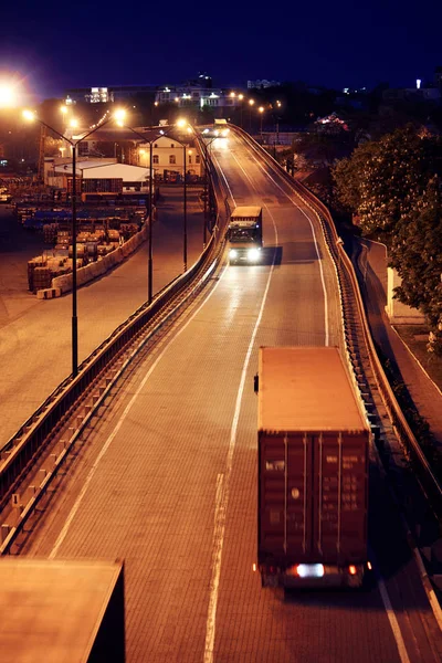 Truck with container rides on the road, freight cars in industrial seaport at night — Stock Photo, Image