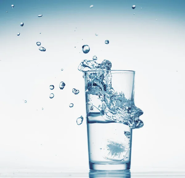 Jedna sklenice vody se šplouchnutím z padající kostky ledu, bílé pozadí, izolovaný objekt — Stock fotografie