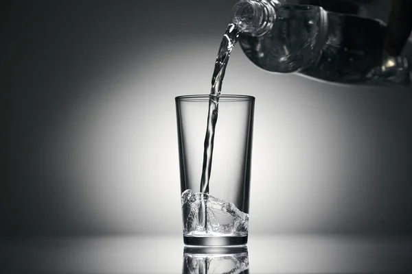 Szénsavas vizet öntök egy pohárba sötét háttérrel. — Stock Fotó