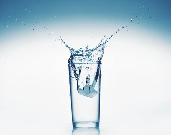 Un bicchiere d'acqua con spruzzi di ghiaccio caduta cubo, sfondo bianco, oggetto isolato — Foto Stock