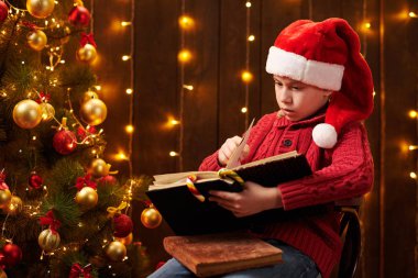 Genç çocuk kitap okuyor, kapalı bir yerde Noel Baba yardımcısı gibi giyinmiş, ışıklarla süslenmiş Xmas ağacının yanında oturuyor.!