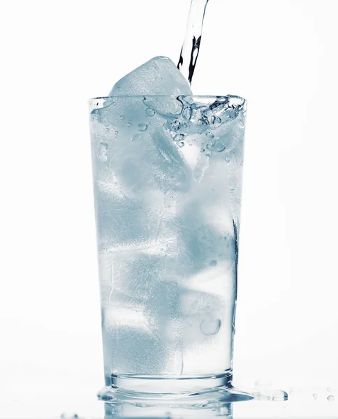 Nalewanie wody do szklanki pełnej kostek lodu, białe tło, niebieski obiekt stonowany — Zdjęcie stockowe