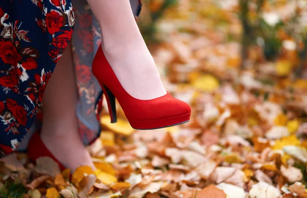 Close up of women's feet shod in red high heels shoes, autumn season, yellow fallen leaves as background — Stock Photo, Image