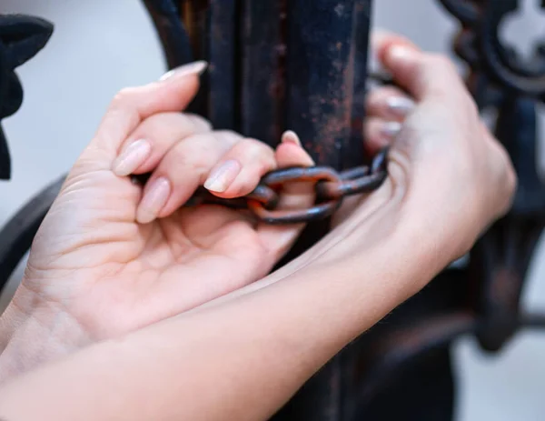 As mãos da mulher segura a corrente em portas de ferro forjado preto — Fotografia de Stock