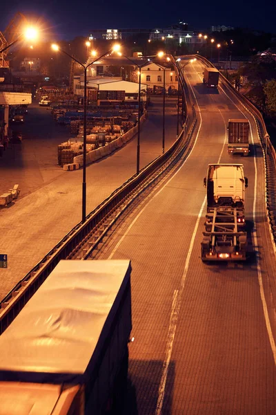 Samochód ciężarowy z przejazdami kontenerowymi po drodze, wagony towarowe w porcie morskim w nocy — Zdjęcie stockowe