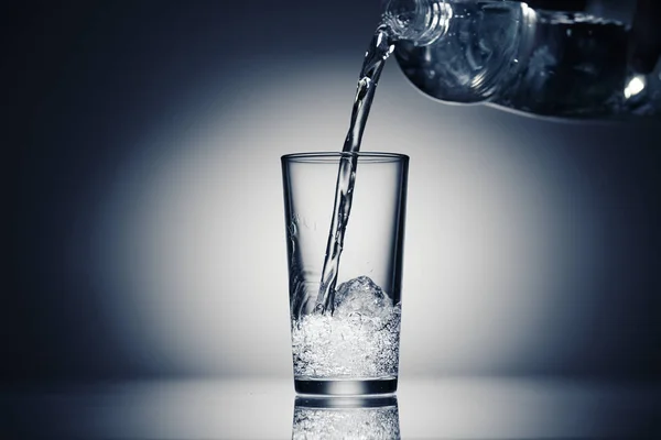 Derramando água espumante em um copo em um fundo azul escuro — Fotografia de Stock